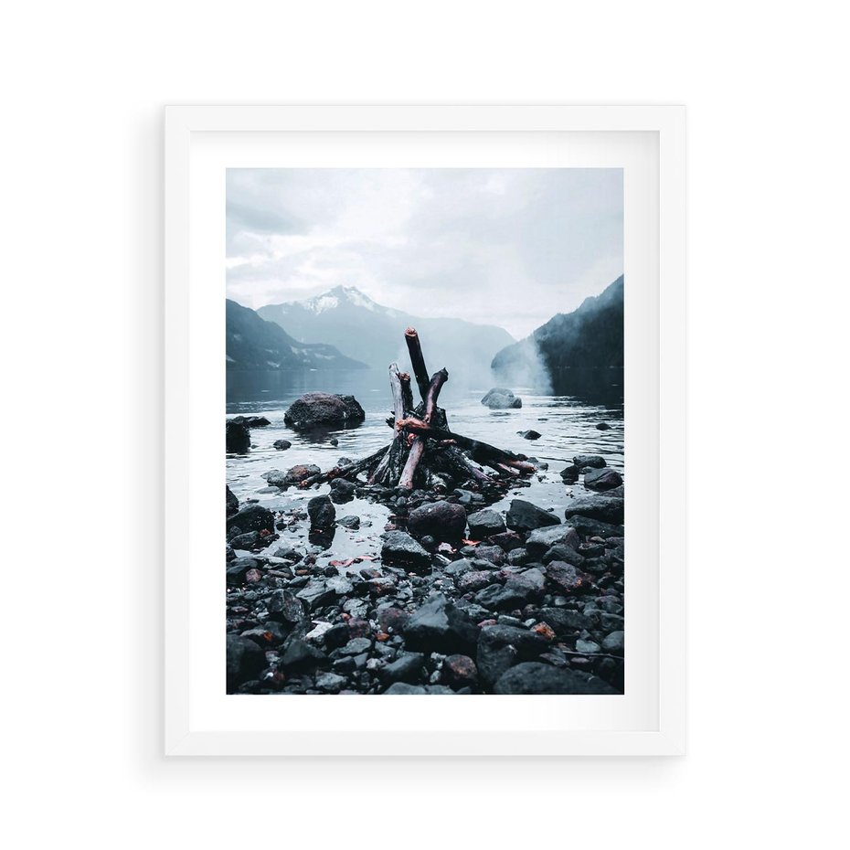 Plakat w ramie 40x50 - To ujęcie jeziora w górach z zgaszonym ogniskiem nad brzegiem, tworząc atmosferę spokoju i refleksji w otoczeniu przyrody. - jezioro w górach, zgaszone ognisko - rama biała