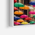 Obraz w ramie 50x70 - Barwna symfonia wyobraźni - fotografia, kolorowe parasolki podwieszone nad ulicą - rama biała