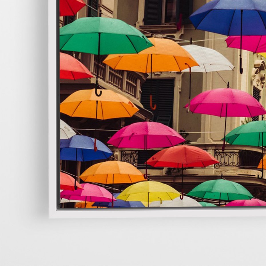 Obraz w ramie 80x120 - Barwna symfonia wyobraźni - fotografia, kolorowe parasolki podwieszone nad ulicą - rama biała