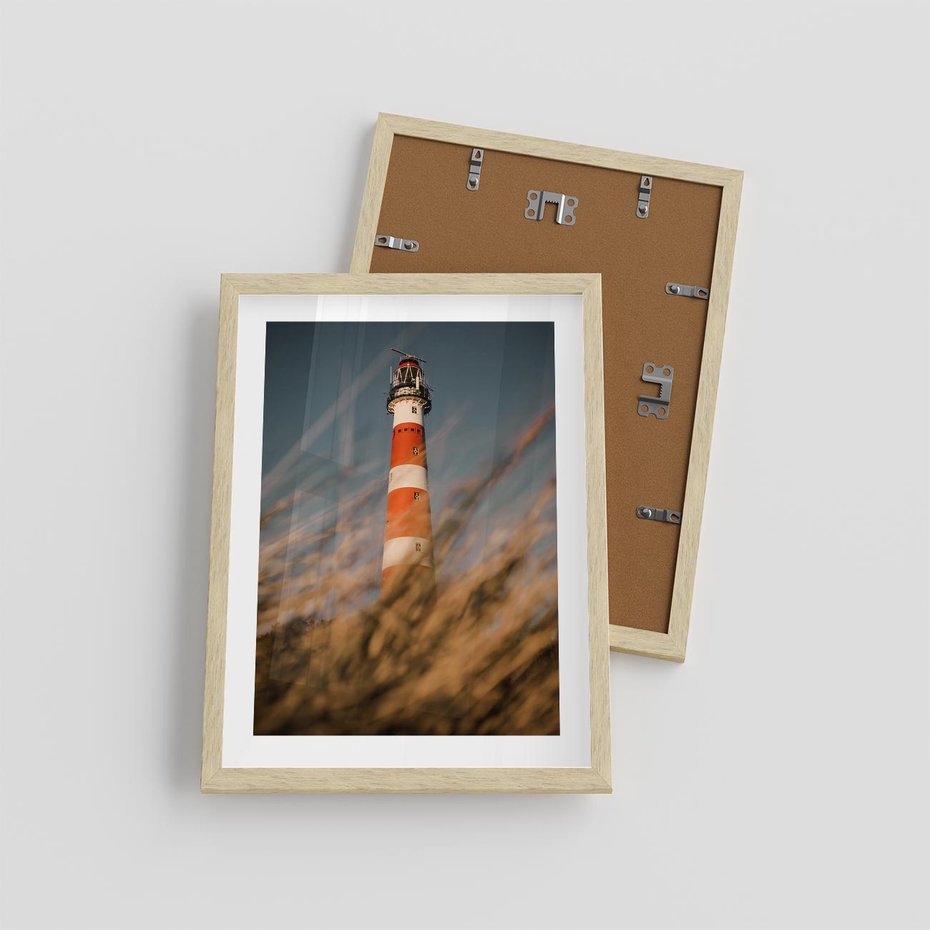 Plakat w ramie 30x40 - Magia nadmorskiego światła - latarnia morska, ujęcie z za trawy - rama drewno