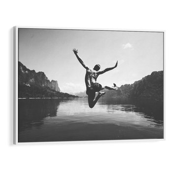 Obraz w ramie 70x50 - Beztroska Chwila - czarno biała fotografia, mężczyzna wesoło wskakuje do keziora w górach - rama biała