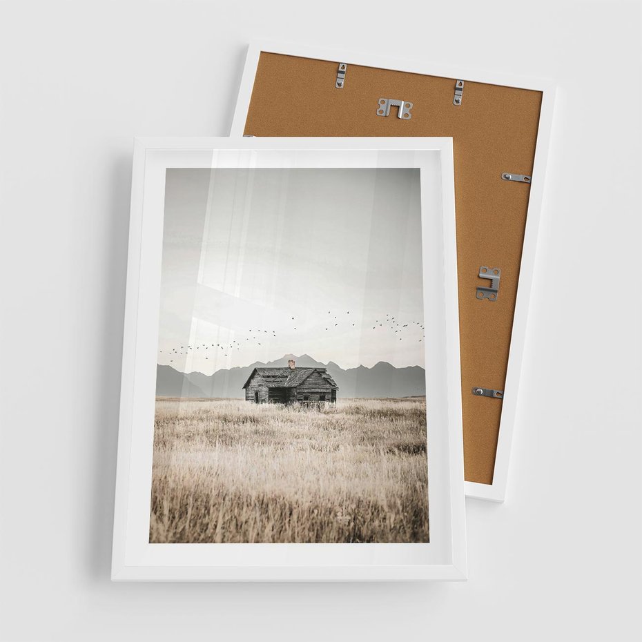 Plakat w ramie 50x70 - Wiejska Idylla - stary drewniany dom w polu suchej trawy, fotografia - rama biała