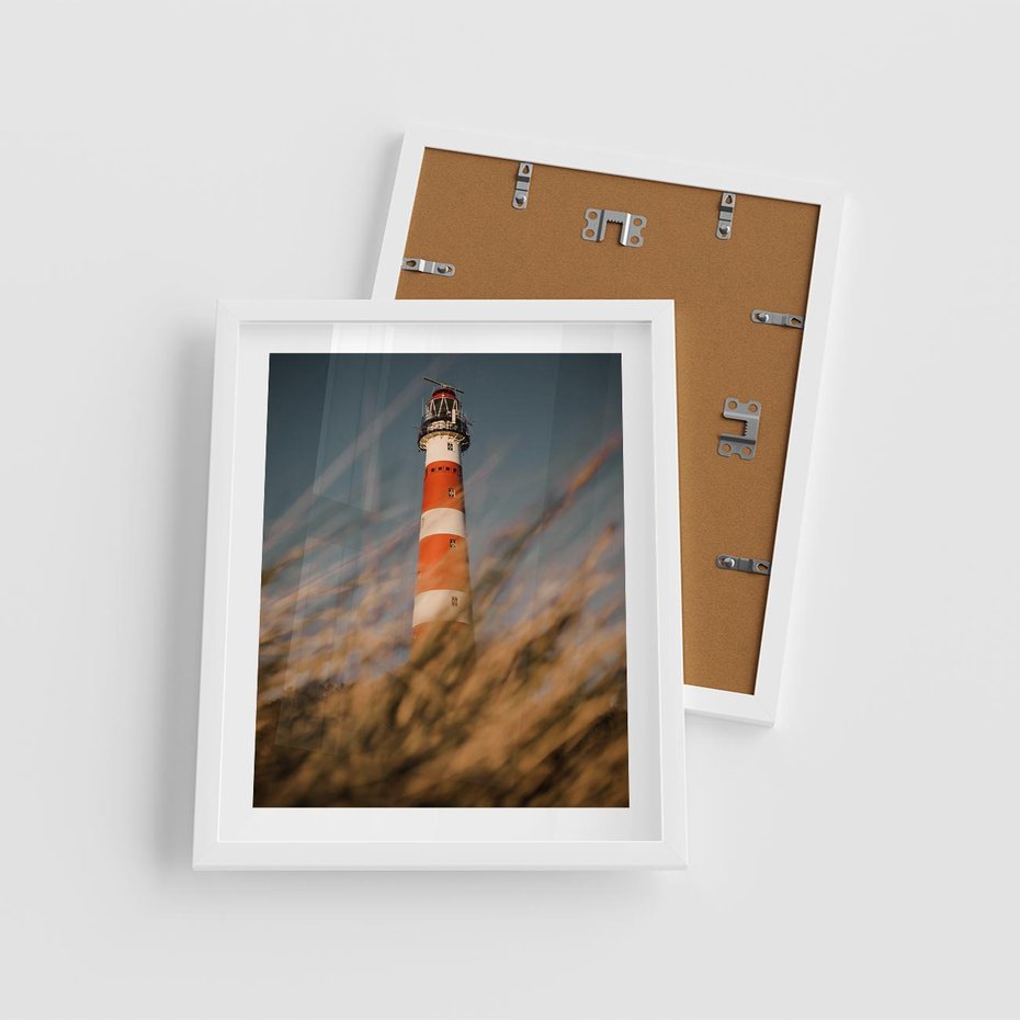 Plakat w ramie 40x50 - Magia nadmorskiego światła - latarnia morska, ujęcie z za trawy - rama biała