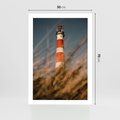 Plakat bez ramy 50x70 - Magia nadmorskiego światła - latarnia morska, ujęcie z za trawy