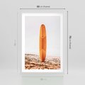 Plakat w ramie 50x70 - Deska w Piasku: Gotowa na Fale - plaża, pomarańczowa deska surfingowa wbita w piasek - rama biała