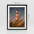 Plakat w ramie 40x50 - Magia nadmorskiego światła - latarnia morska, ujęcie z za trawy - rama czarna