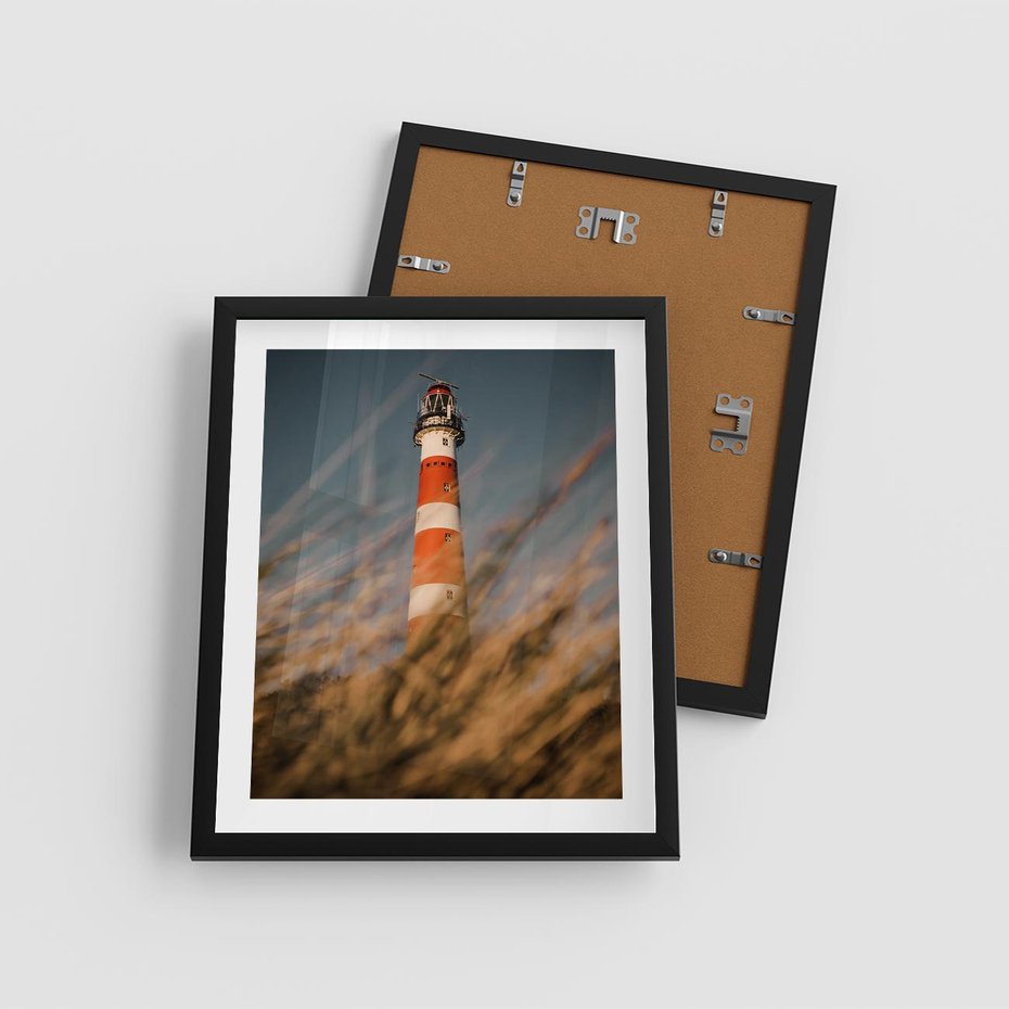 Plakat w ramie 40x50 - Magia nadmorskiego światła - latarnia morska, ujęcie z za trawy - rama czarna