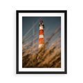 Plakat w ramie 40x50 - Magia nadmorskiego światła - latarnia morska, ujęcie z za trawy - rama czarna