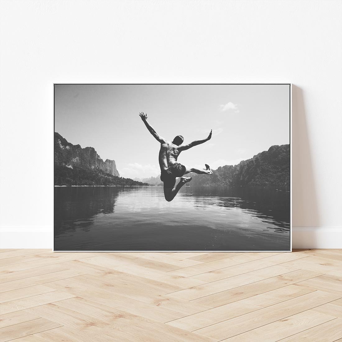 Obraz w ramie 70x50 - Beztroska Chwila - czarno biała fotografia, mężczyzna wesoło wskakuje do keziora w górach - rama biała