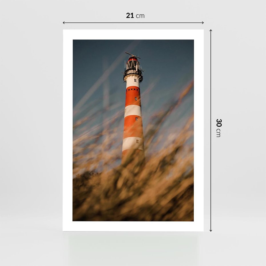 Plakat bez ramy 21x30 - Magia nadmorskiego światła - latarnia morska, ujęcie z za trawy