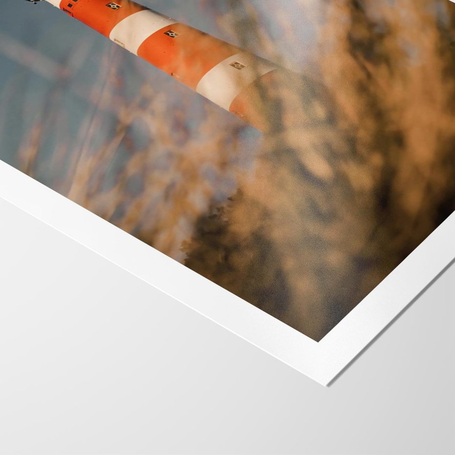 Plakat bez ramy 21x30 - Magia nadmorskiego światła - latarnia morska, ujęcie z za trawy
