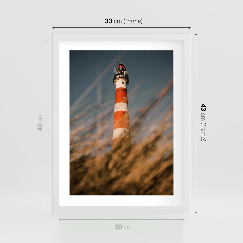 Plakat w ramie 30x40 - Magia nadmorskiego światła - latarnia morska, ujęcie z za trawy - rama biała