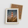 Plakat w ramie 40x50 - Magia nadmorskiego światła - latarnia morska, ujęcie z za trawy - rama drewno