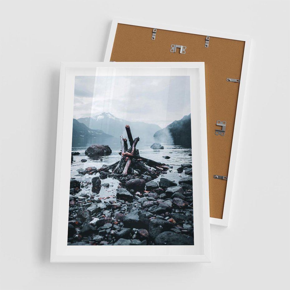 Plakat w ramie 50x70 - To ujęcie jeziora w górach z zgaszonym ogniskiem nad brzegiem, tworząc atmosferę spokoju i refleksji w otoczeniu przyrody. - jezioro w górach, zgaszone ognisko - rama biała