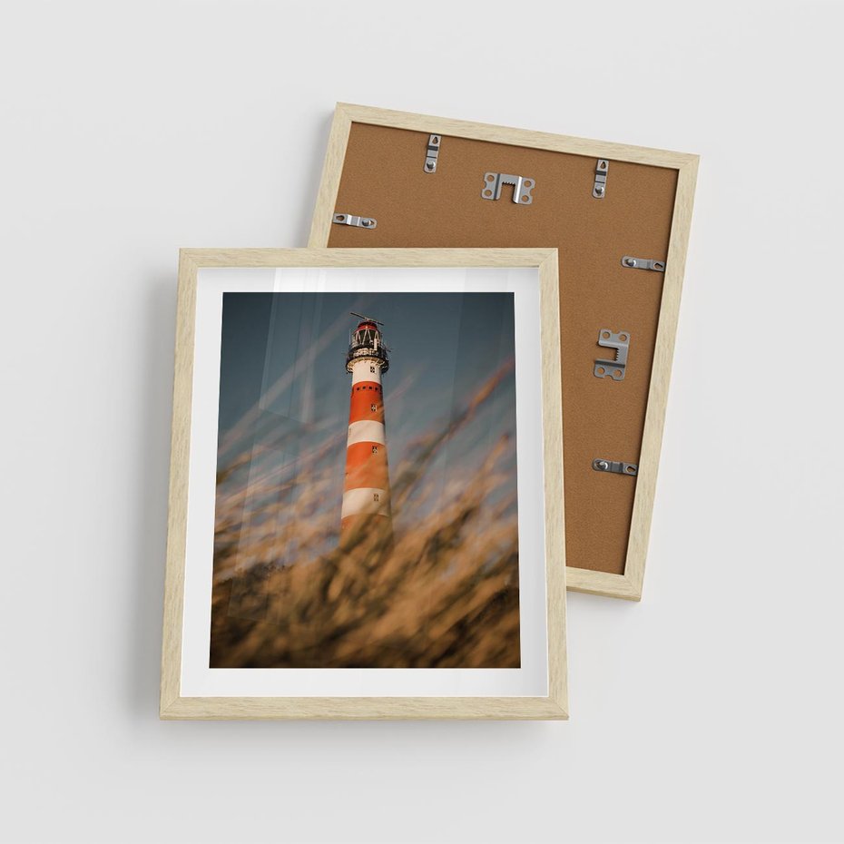Plakat w ramie 40x50 - Magia nadmorskiego światła - latarnia morska, ujęcie z za trawy - rama drewno
