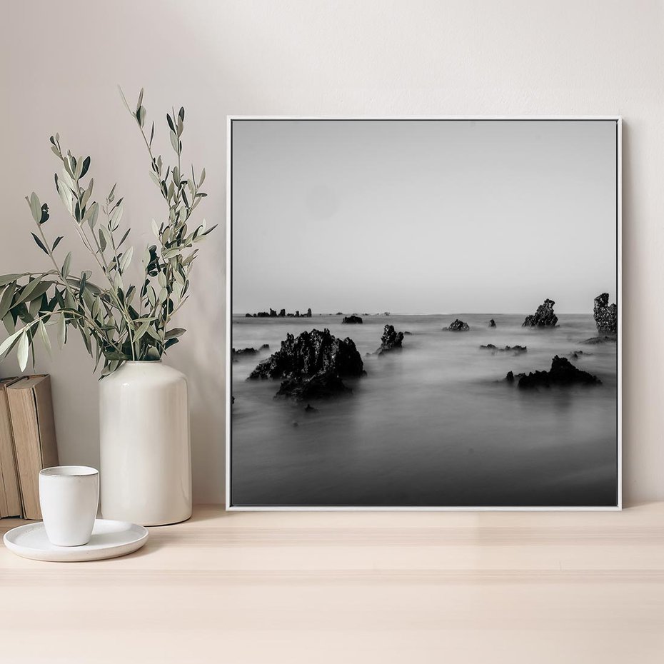 Obraz w ramie 80x80 - Harmonia świateł i cieni - zamglona dzika plaża, skały na plaży - rama biała