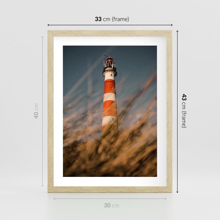 Plakat w ramie 30x40 - Magia nadmorskiego światła - latarnia morska, ujęcie z za trawy - rama drewno
