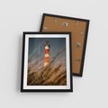 Plakat w ramie 40x50 - Magia nadmorskiego światła - latarnia morska, ujęcie z za trawy - rama czarna