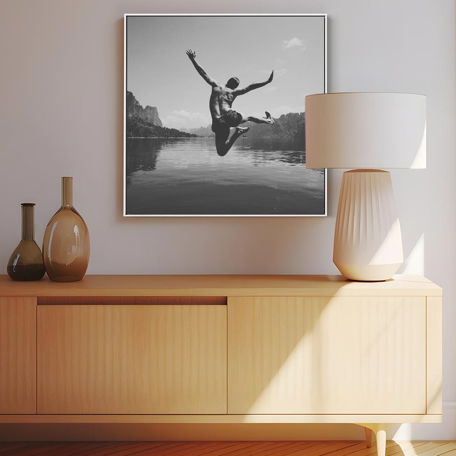 Obraz w ramie 50x50 - Beztroska Chwila - czarno biała fotografia, mężczyzna wesoło wskakuje do keziora w górach - rama biała