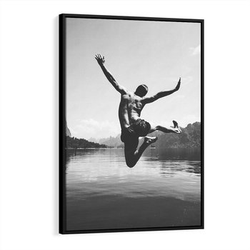 Obraz w ramie 70x100 - Beztroska Chwila - czarno biała fotografia, mężczyzna wesoło wskakuje do keziora w górach - rama czarna
