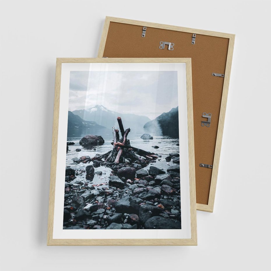 Plakat w ramie 50x70 - To ujęcie jeziora w górach z zgaszonym ogniskiem nad brzegiem, tworząc atmosferę spokoju i refleksji w otoczeniu przyrody. - jezioro w górach, zgaszone ognisko - rama drewno