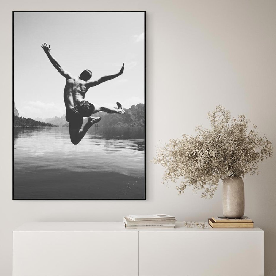 Obraz w ramie 70x100 - Beztroska Chwila - czarno biała fotografia, mężczyzna wesoło wskakuje do keziora w górach - rama czarna