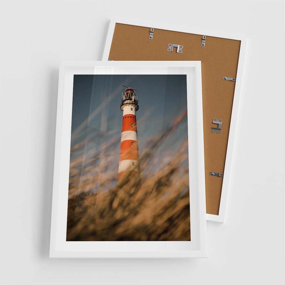 Plakat w ramie 50x70 - Magia nadmorskiego światła - latarnia morska, ujęcie z za trawy - rama biała