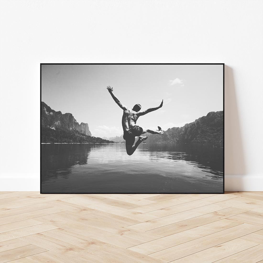 Obraz w ramie 100x70 - Beztroska Chwila - czarno biała fotografia, mężczyzna wesoło wskakuje do keziora w górach - rama czarna